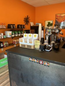 The view of our cafe space from the front door. You can see our front counter with cups and espresso machine in the foreground. In the background are our retail shelves with bags of coffee for sale.