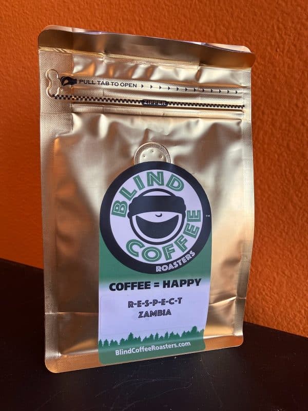 Photo showing a gold 8 ounce bag of Blind Coffee with BCR logo and label that says R-E-S-P-E-C-T Zambia