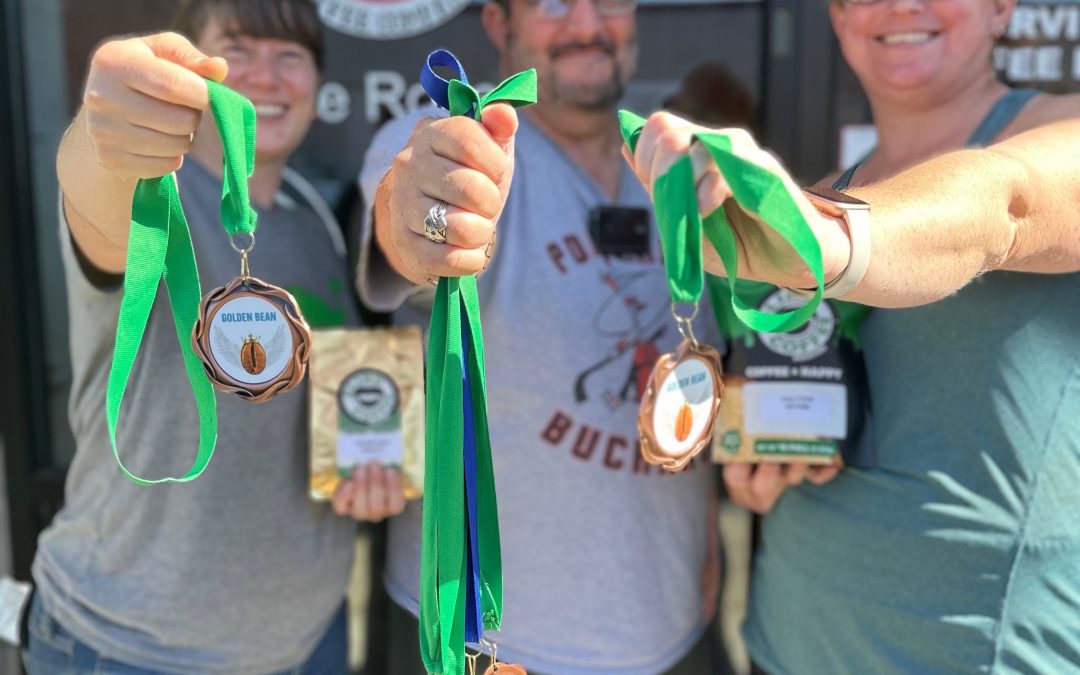 Photo of 3 of the BCR Crew in front of the coffee shop holding up medals and award winning bags of coffee.